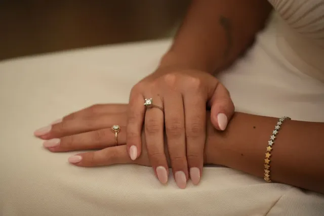 Natural nude manicured nails on resting hands with delicate rings