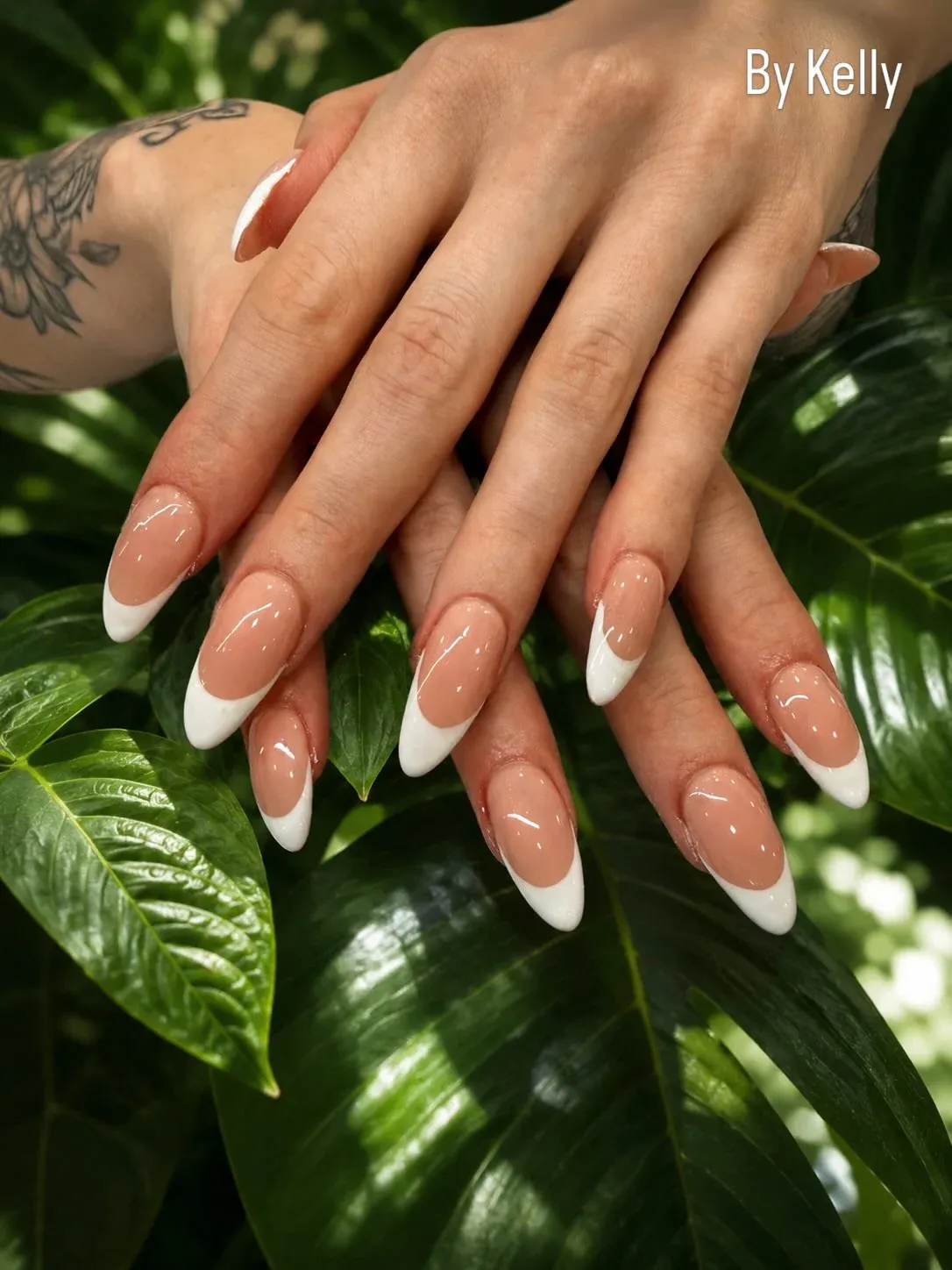 Glossy white French tips on long almond-shaped nails resting on tropical leaves