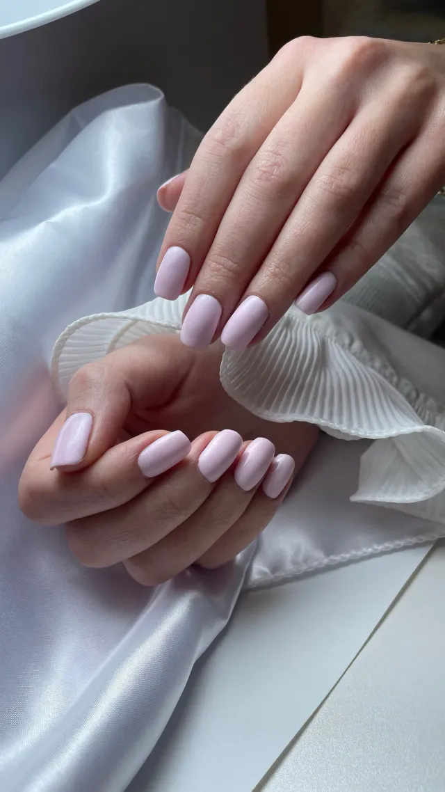 Glossy soft-pink gel manicure on square nails resting on white silk