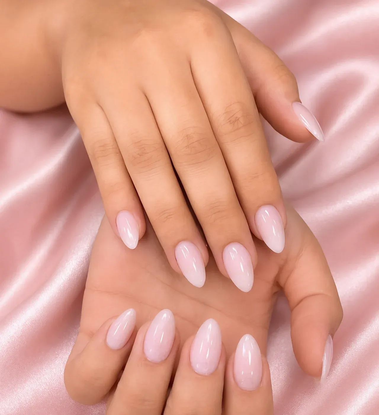 Glossy milky-pink almond nails resting on soft pink satin