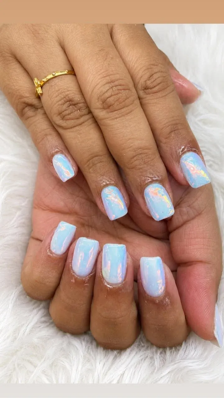 Short square nails finished in pearlescent sky blue chrome polish on a soft fur backdrop